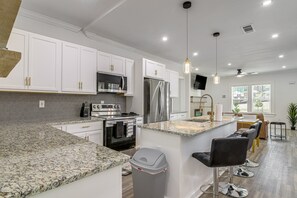 Een moderne keuken met witte kastjes, roestvrijstalen apparatuur, granieten aanrechtbladen en een centraal eiland met barkrukken.
