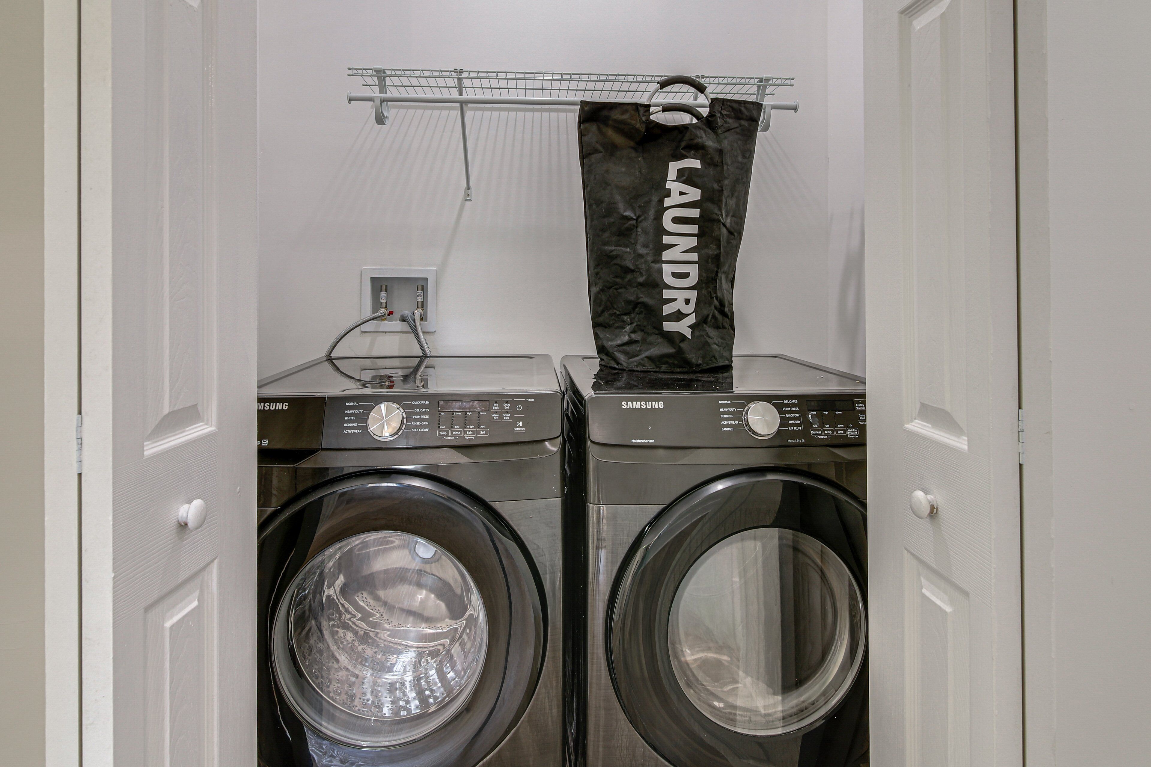 Two front-loading washing machines with control panels, a power outlet, and a metal rack above them.