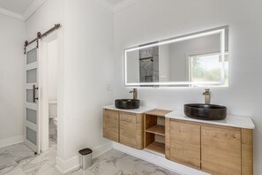 Een badkamer met een wit wastafelmeubel, twee zwarte wasbakken, een houten kast, een marmeren vloer en een witte douche met een glazen deur.