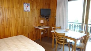 Ein Zimmer mit einem Bett, einem Schreibtisch mit Stuhl, einem Fernseher und einem Fenster mit Vorhängen.