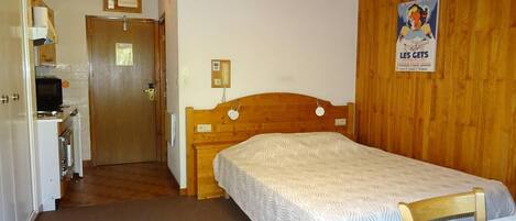 A room with a bed, wooden headboard, a small desk with a chair, and a poster on the wall.