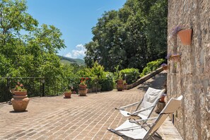 Eine Terrasse mit Backsteinpflasterung, Kübelpflanzen und zwei weißen Lounge-Stühlen.