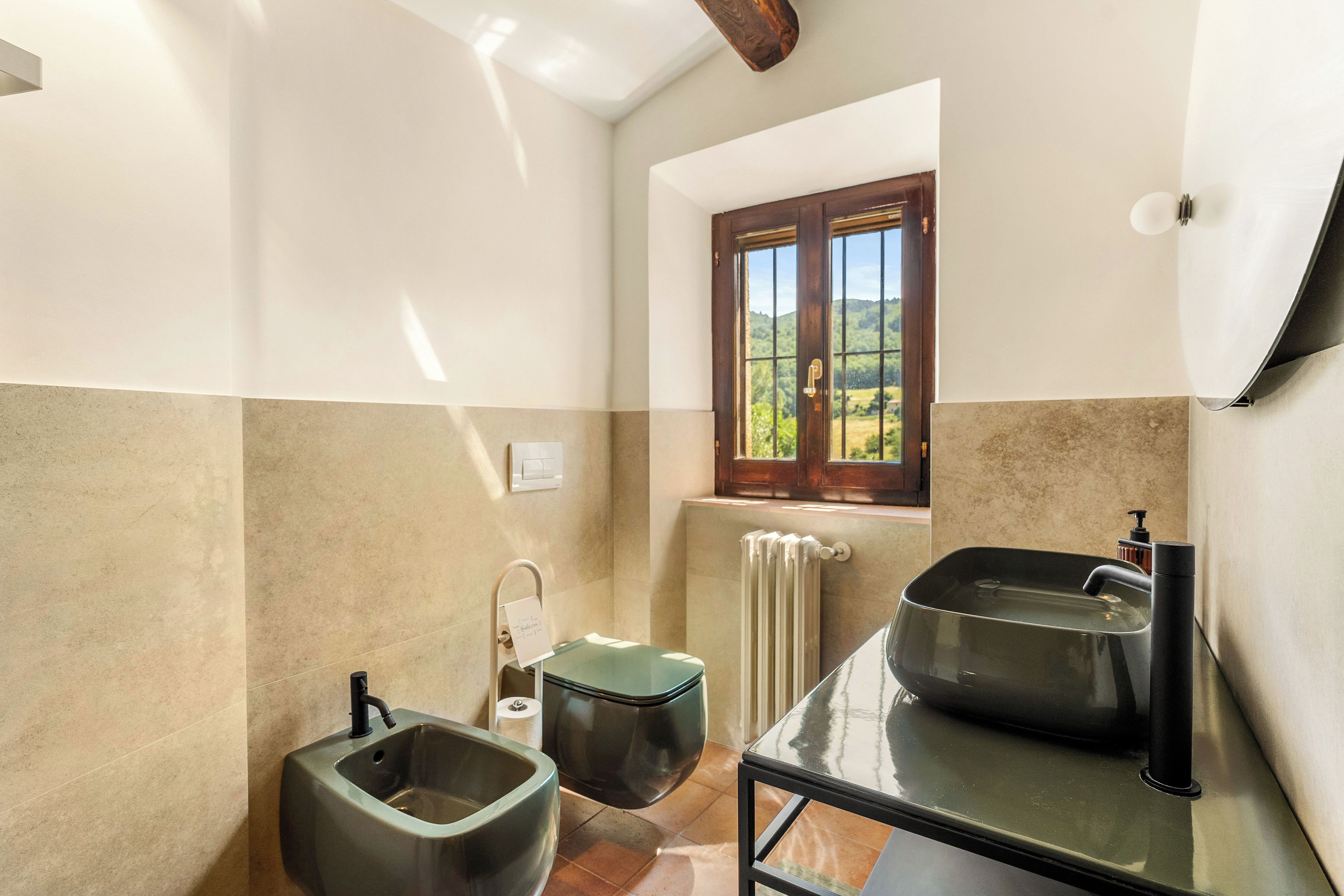 A bathroom with a window, a radiator, a sink, and a toilet.