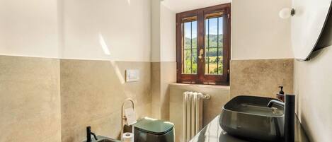 A bathroom with a window, a radiator, a sink, and a toilet.