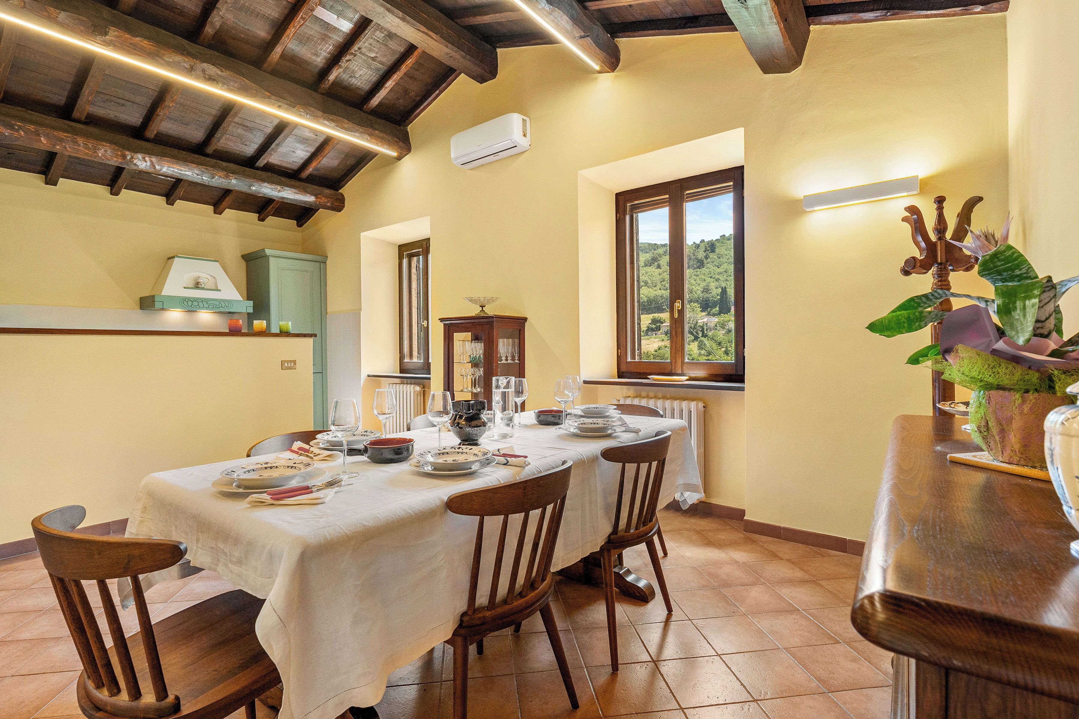 A dining area with a table set for a meal, wooden chairs, a window with a view, and a radiator.