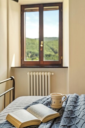 Ein Zimmer mit einem Bett, einem Fenster mit Blick auf Grünflächen, einem Heizkörper und einem Buch mit einer Tasse darauf.