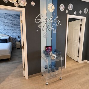 Une chambre d’hôtel avec un lit, une table de chevet, une petite table, un mur orné d’une boule à facettes et une pancarte sur laquelle on peut lire : « En selle ! »