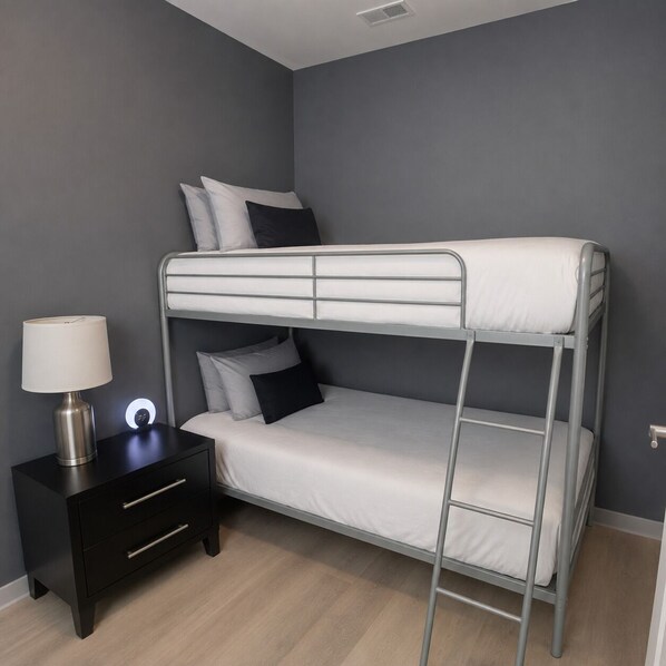 Un lit superposé avec une table de chevet et une lampe, dans une pièce aux murs gris et au plancher en bois.