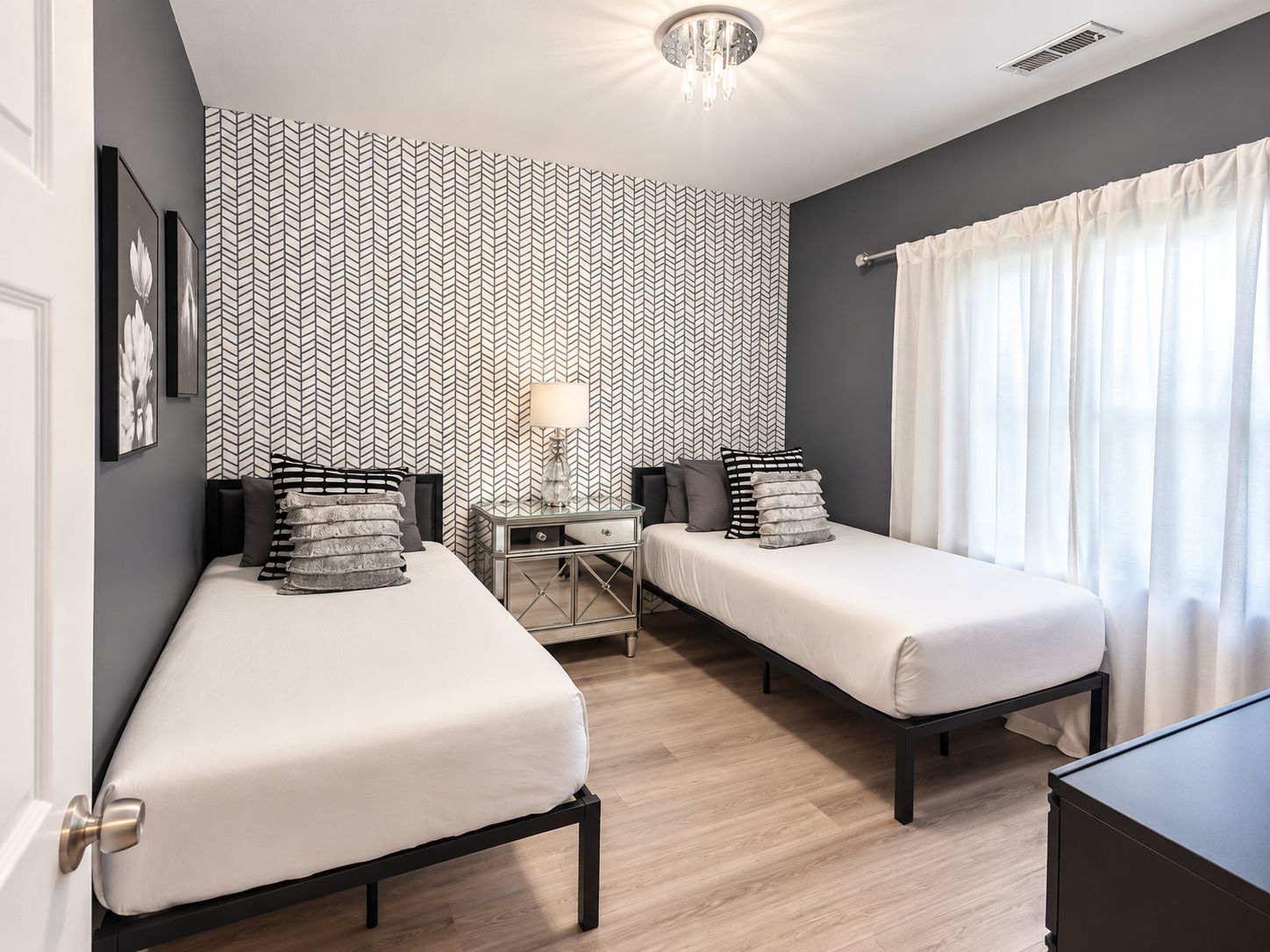 A hotel room with two beds, a bedside table, a lamp, and a window with curtains.