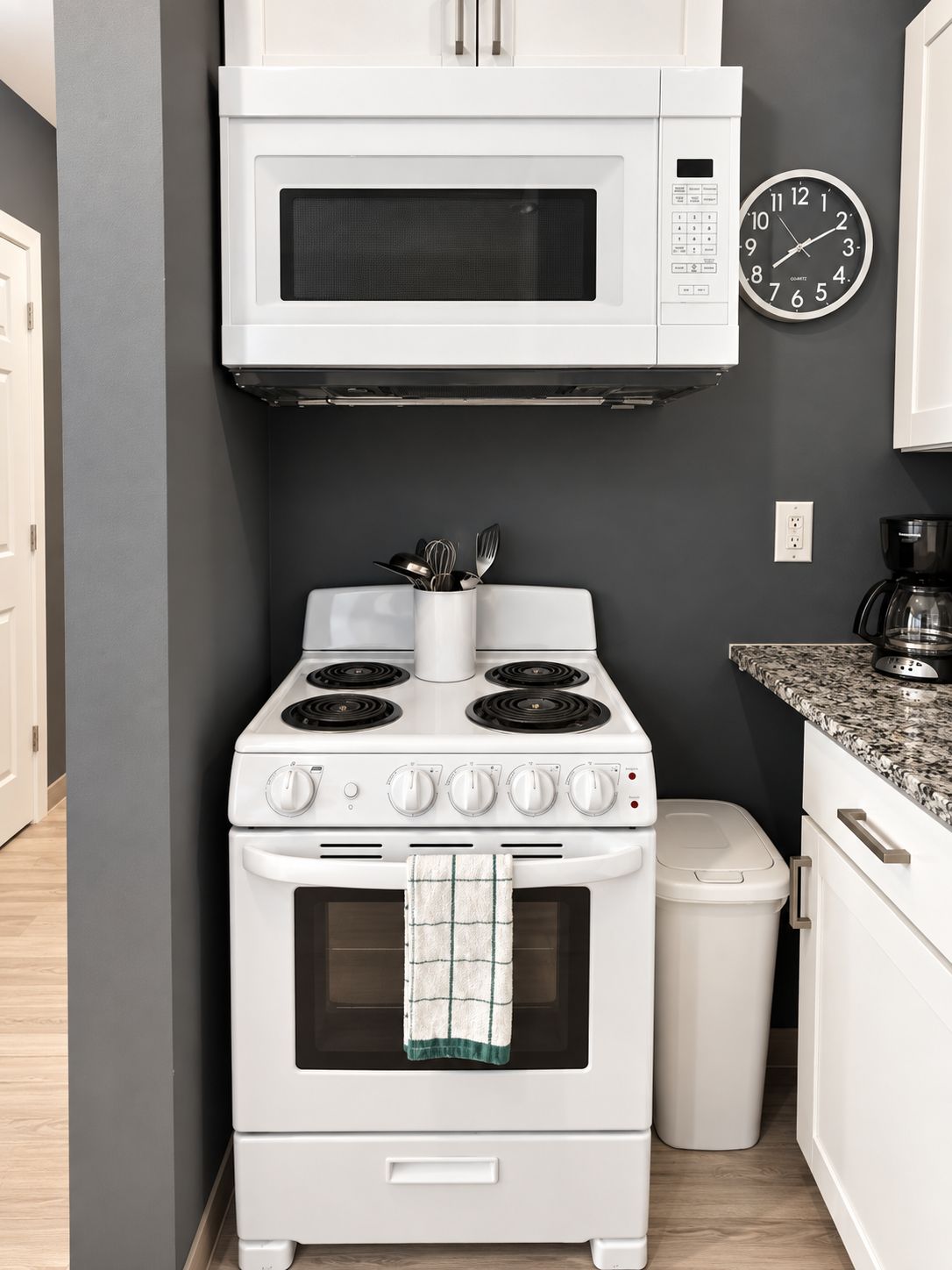 Une cuisine avec un four blanc, un four à micro-ondes placé au-dessus, et une horloge au mur.