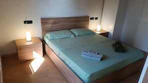 A neatly made bed with a light green bedspread and pillows, two bedside tables with lamps, and a wooden headboard. - Abby's House - Milan Hub – Stylish Central Apartment Near the Station (Gallarate)