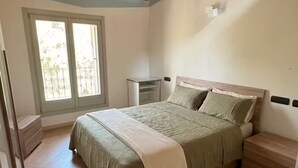 Un dormitorio con techo de madera, una cama con colcha verde, una mesita de noche y una ventana con vistas a la vegetación.