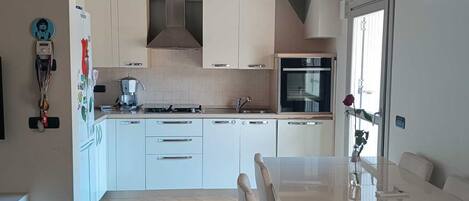 Una cocina moderna con armarios blancos, una isla central y un comedor con mesa y sillas blancas.