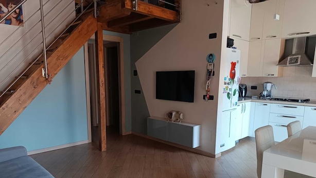 Un espacio habitable moderno con una escalera de madera, un televisor de pantalla plana y una zona de cocina.