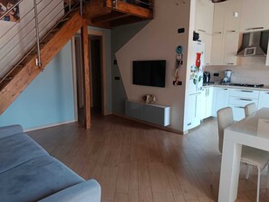 A modern living space with a wooden staircase, a flat-screen TV, and a kitchen area. - Abby's House - Milan Hub – Stylish Central Apartment Near the Station (Gallarate)