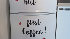 Un refrigerador con una calcomanía de una flor y el mensaje 'OK, pero primero café!'.