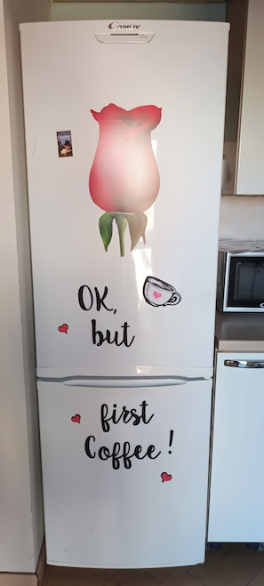 Een koelkast met een bloemensticker en de tekst 'OK, maar eerst koffie!'.