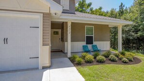 A single-story house with a covered porch, a garage, and a well-maintained lawn with flowers. - Cozy 3-bedroom cottage in delightful Pensacola. Only a few mins from the beach. (Pensacola)