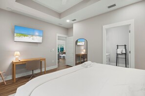 A hotel room with a bed, a desk, a chair, a TV, and a bathroom visible through an open door. - Cozy 3-bedroom cottage in delightful Pensacola with AC. 10 Mins from the beach. (Pensacola)