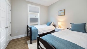 A bedroom with two beds, a ceiling fan, a nightstand with a lamp, and a painting on the wall. - Cozy 3-bedroom cottage in delightful Pensacola. Only a few mins from the beach. (Pensacola)