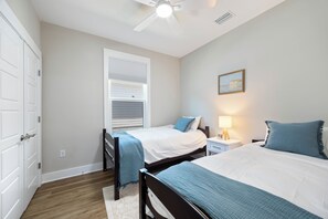 A bedroom with two beds, a ceiling fan, a nightstand with a lamp, and a painting on the wall. - Cozy 3-bedroom cottage in delightful Pensacola. Only a few mins from the beach. (Pensacola)