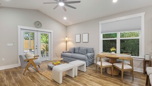 A modern living room with a grey sofa, wooden coffee table, and a dining area with a round table and chairs. - Cozy 3-bedroom cottage in delightful Pensacola. Only a few mins from the beach. (Pensacola)