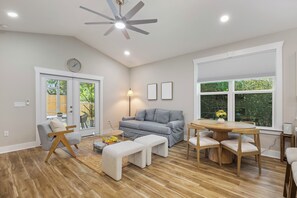 A modern living room with a grey sofa, wooden coffee table, and a dining area with a round table and chairs. - Cozy 3-bedroom cottage in delightful Pensacola. Only a few mins from the beach. (Pensacola)