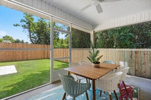A covered patio with a table and chairs, a ceiling fan, and a view of a grassy backyard.