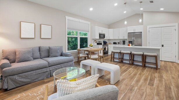 A modern living room with a grey sofa, a glass coffee table, and a white pouf. - Cozy 3-bedroom cottage in delightful Pensacola. Only a few mins from the beach. (Pensacola)