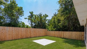 A backyard with a wooden fence, a grassy lawn, and a white tiled area. - Cozy 3-bedroom cottage in delightful Pensacola. Only a few mins from the beach. (Pensacola)
