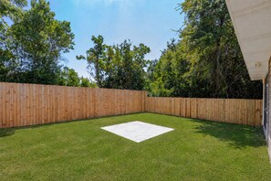 A backyard with a wooden fence, a grassy lawn, and a white tiled area. - Cozy 3-bedroom cottage in delightful Pensacola. Only a few mins from the beach. (Pensacola)