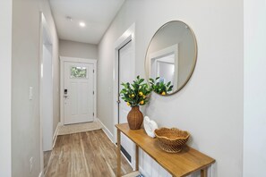 A hallway with a wooden floor, a white door, a mirror, and a wicker basket on a wooden console.