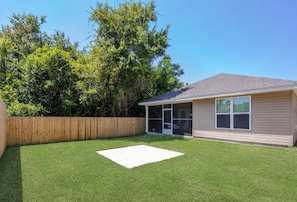 A residential property with a fenced backyard, a patio area, and a house with large windows. - Cozy 3-bedroom cottage in delightful Pensacola with AC. 10 Mins from the beach. (Pensacola)