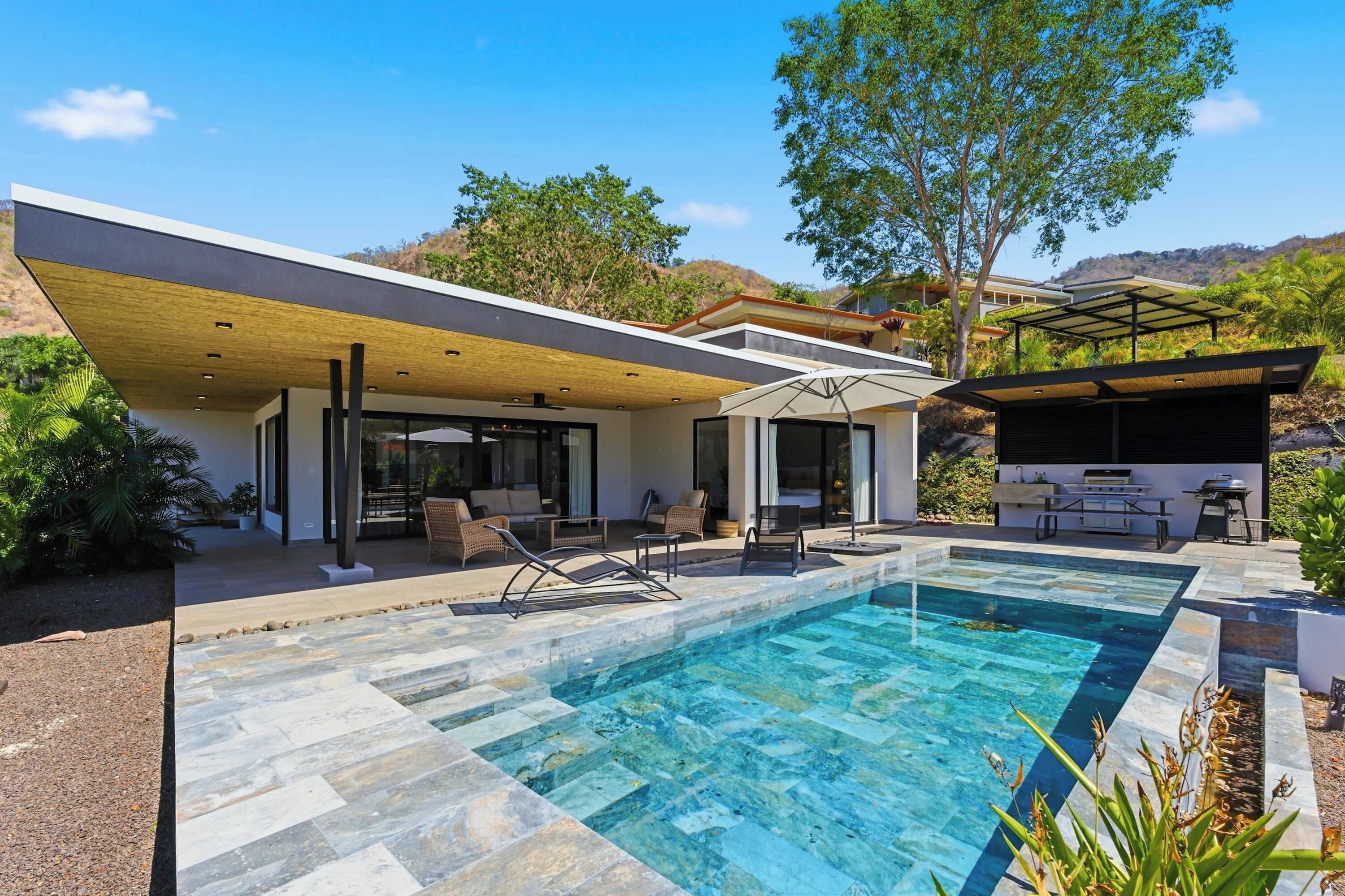 A modern house with a swimming pool, outdoor seating, and a barbecue area.