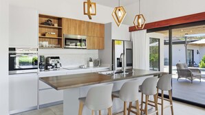 A modern kitchen with a central island, bar stools, a coffee machine, and a view of the outdoor patio. - Luxury Villa + Casita in Mar Vista (Playa Brasilito)