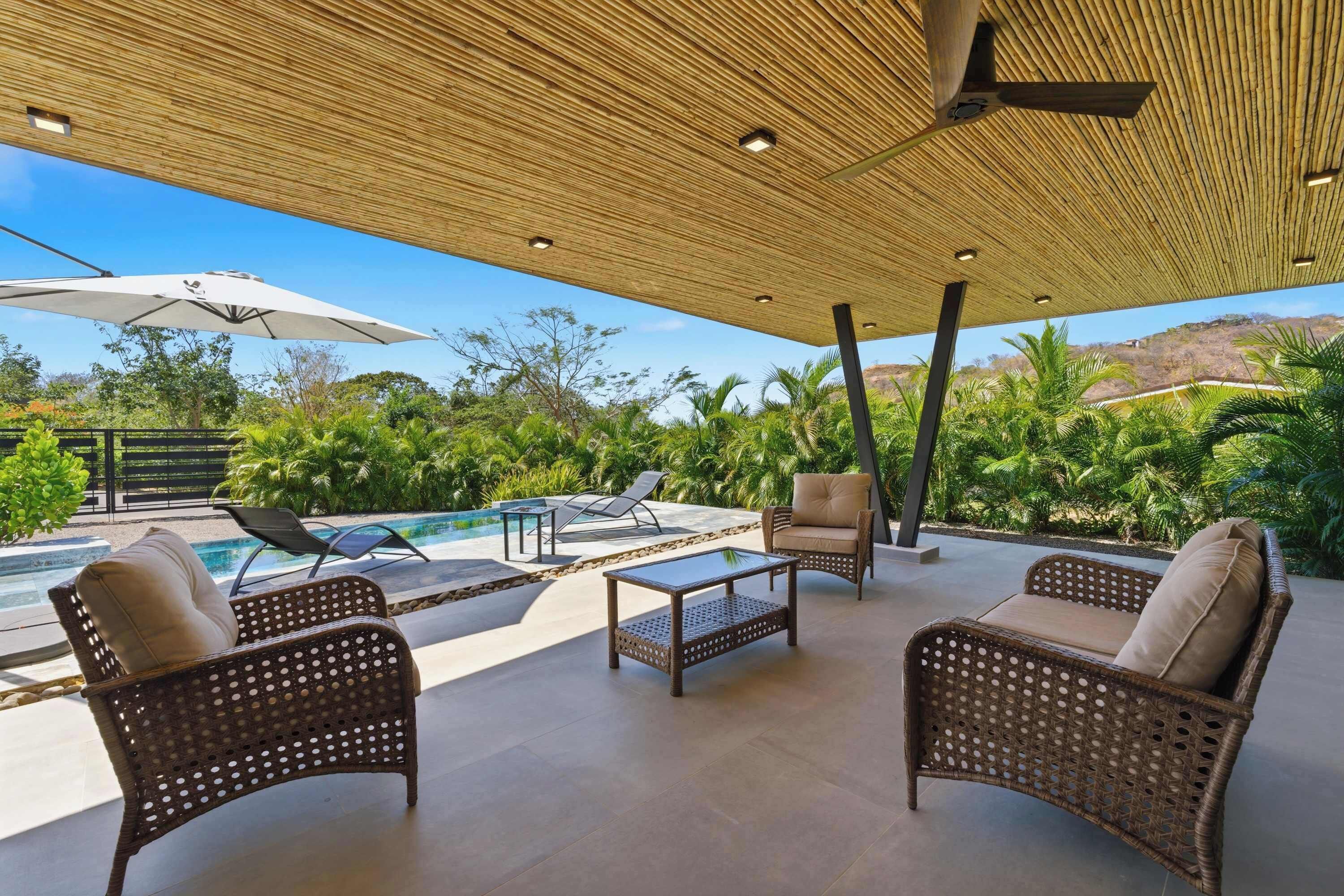 An outdoor patio with wicker furniture, a pool, and a view of the surrounding landscape.