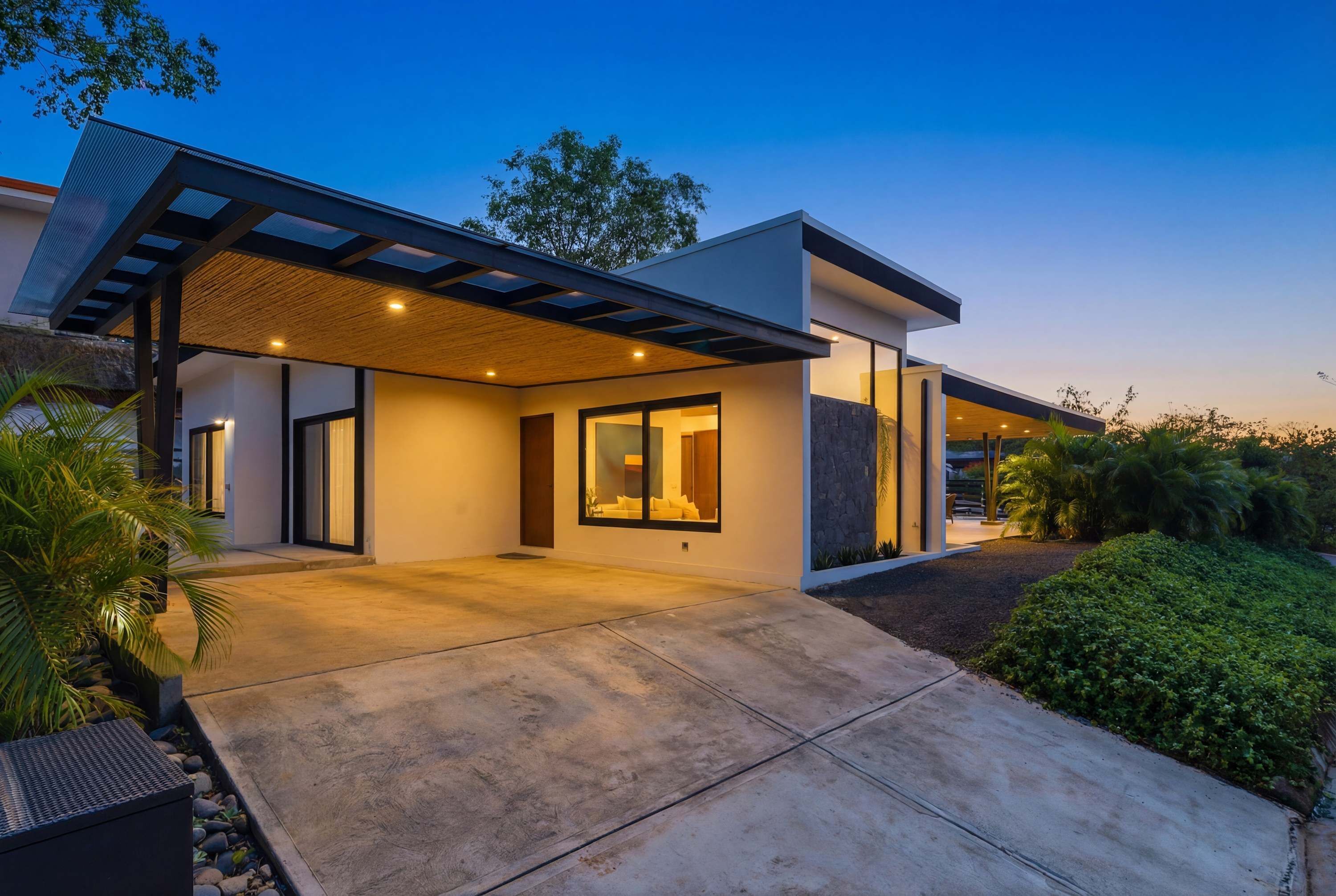Une maison moderne dotée d’un patio couvert, de grandes fenêtres et d’un jardin bien entretenu.