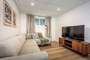 Ein modernes Wohnzimmer mit einem Ecksofa, einem Flachbildfernseher, einer Holzunterhaltungseinheit und zwei gerahmten Bildern an der Wand.