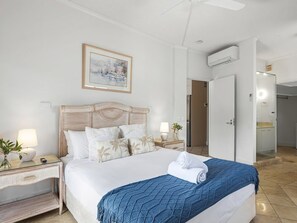 Ett hotellrum med en säng, ett nattduksbord, en lampa, en inramad tavla på väggen och en luftkonditioneringsanläggning.