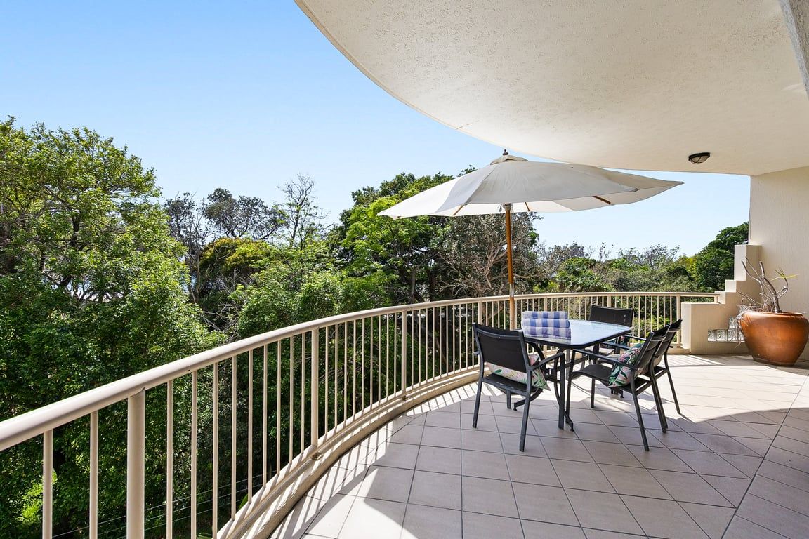 An outdoor balcony with a table and chairs, a large umbrella, and a potted plant.