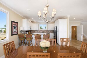 A spacious kitchen with white cabinets, a stainless steel refrigerator, and a dining area with a wooden table and chairs. - Sea Dawg Pool Elevator, Gulf view (Saint George Island)