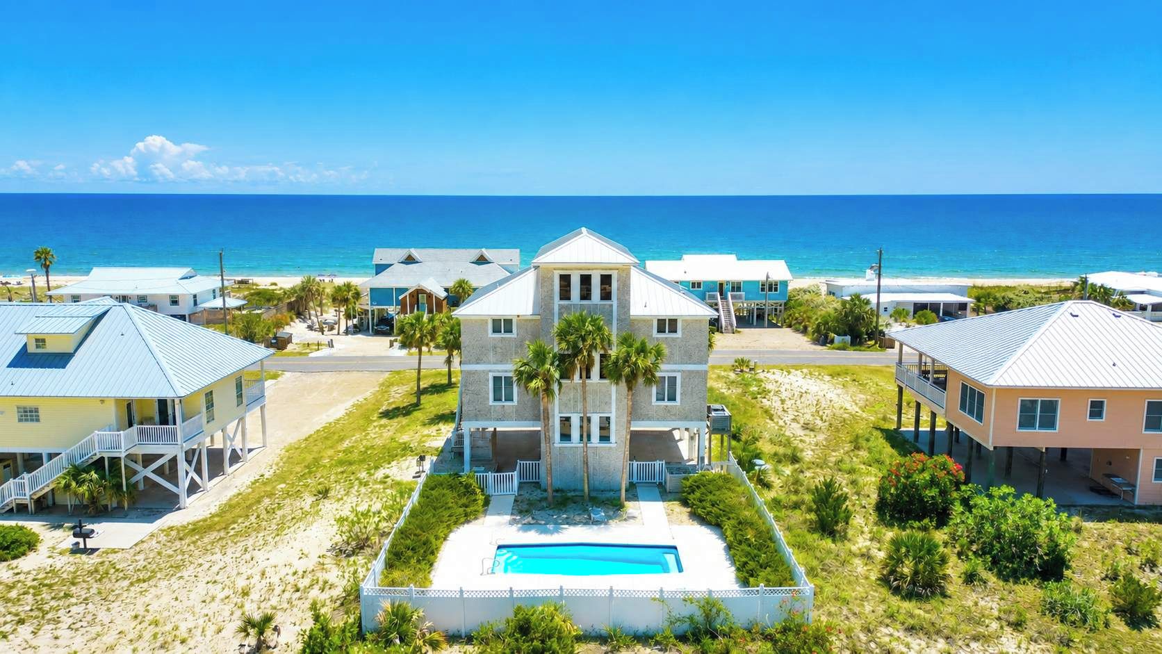A beachfront property with a central building, a swimming pool, and a view of the ocean.