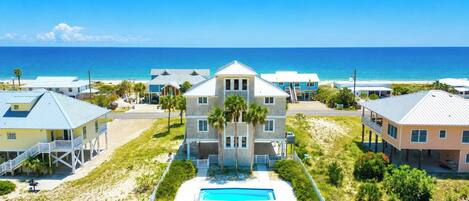 A beachfront property with a central building, a swimming pool, and a view of the ocean.