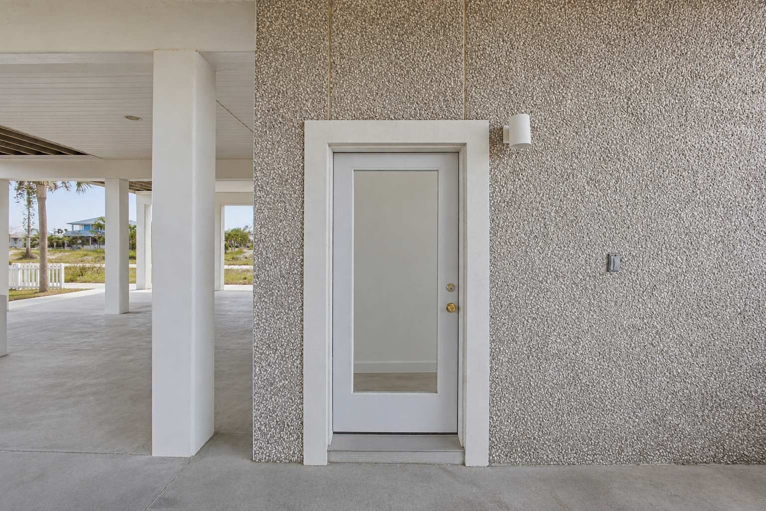 A white door with a textured wall beside it, a white pillar, and a light fixture on the wall.