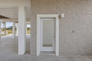 Una porta blanca amb una paret amb relleu al costat, un pilaret i una làmpada a la paret.