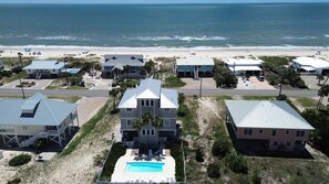 Een kustgebied met woningen, een zwembad en een strand op de achtergrond.
