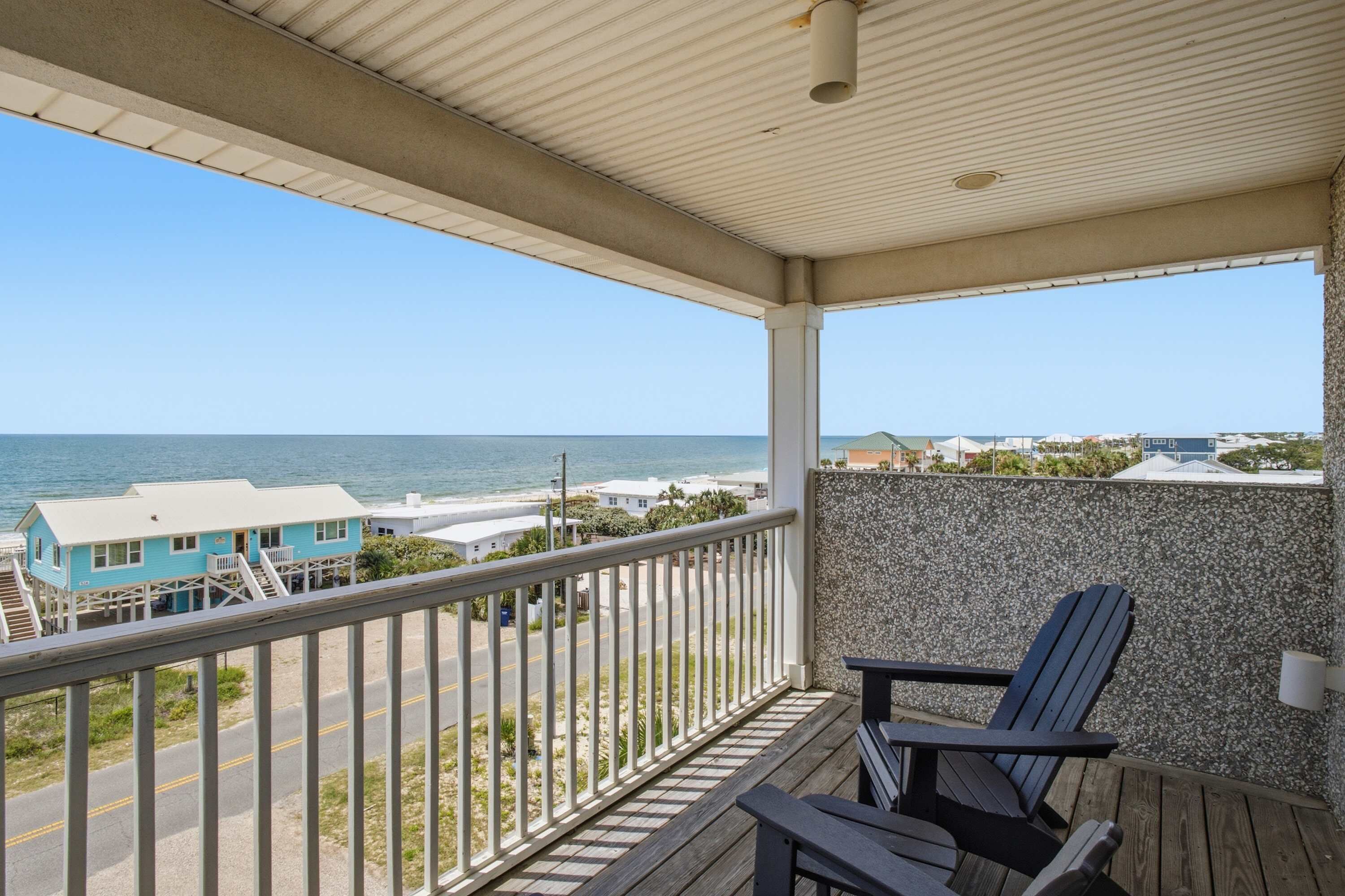 A balcony with a view of the beach and ocean, wooden deck, and a chair.