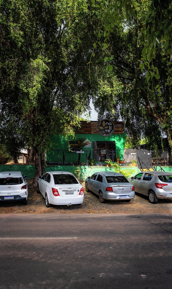 A parking area with four cars, a building with a green facade, and trees providing shade.
