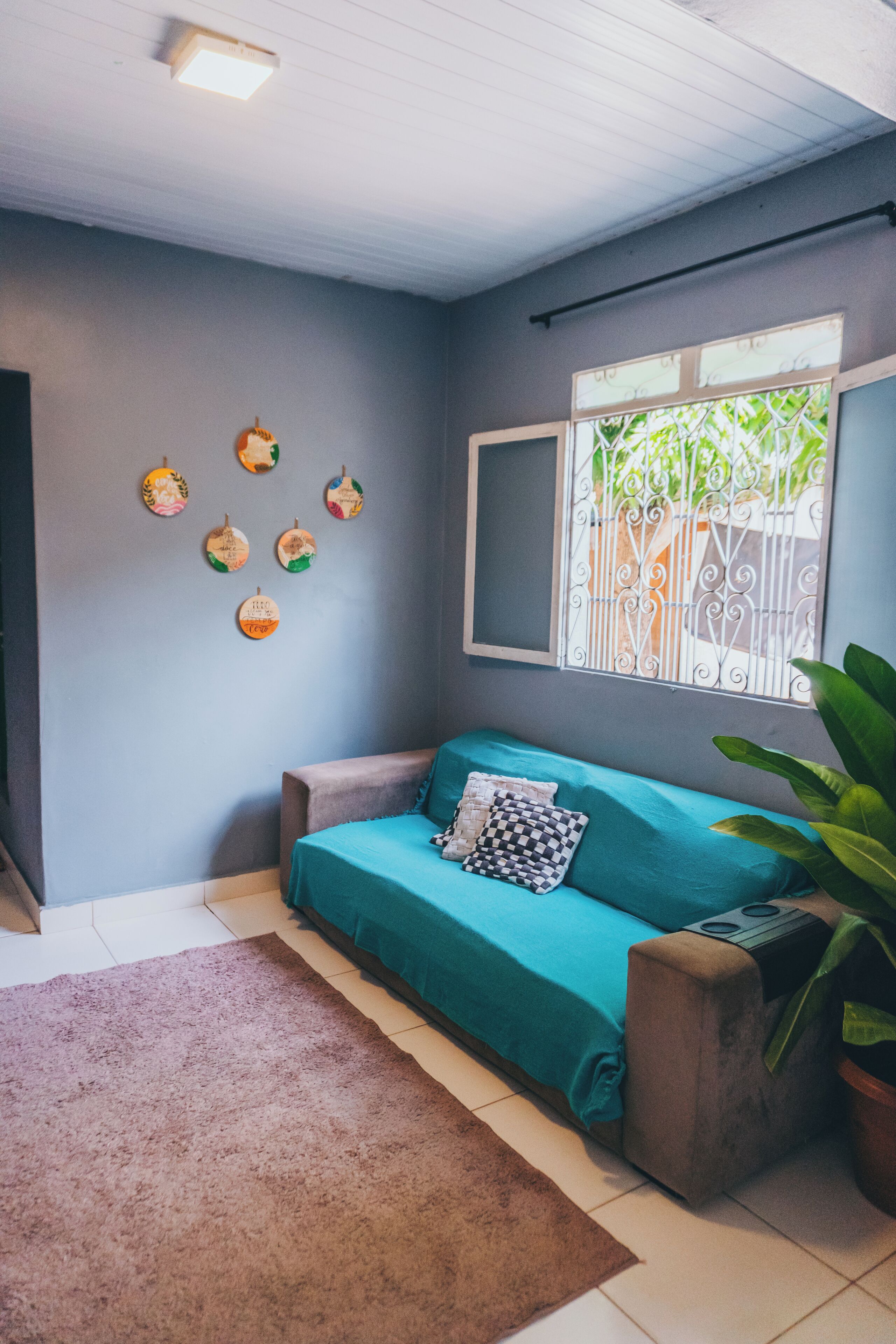A room with a teal sofa, a brown rug, and a window with decorative metal bars.