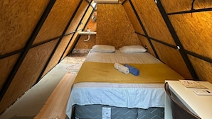 Une chambre mansardée chaleureuse, avec un plafond en pente, un lit avec un matelas et des oreillers, une table de chevet et un luminaire suspendu.